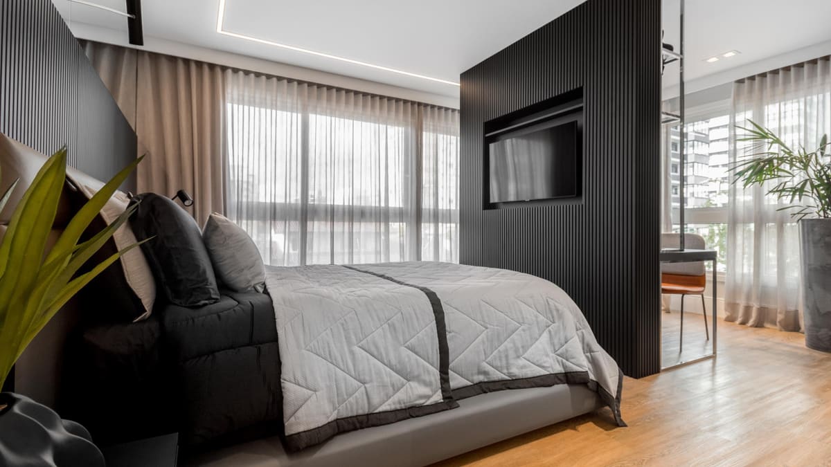 Bedroom with a black slatted partition holding a TV, sheer curtains and a wood floor