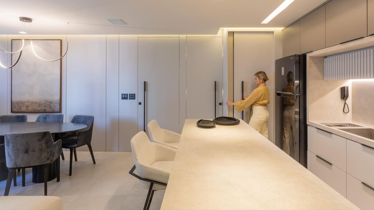 Pale kitchen with a long stone island, tall handleless cabinets and a round dining table