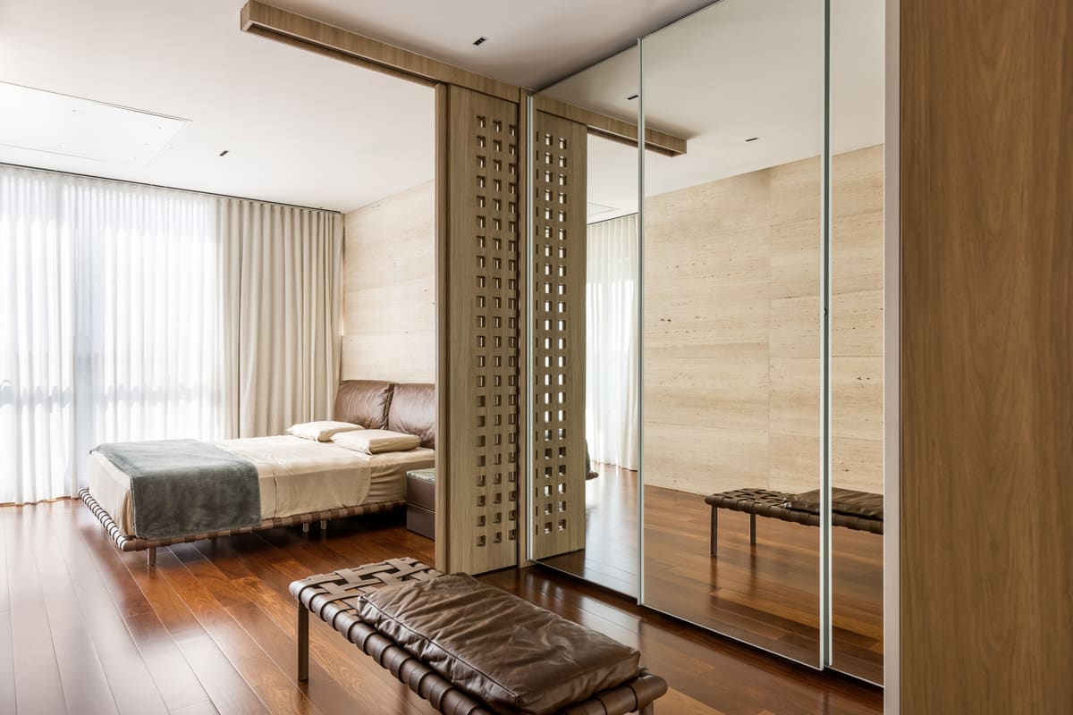 Bedroom behind sliding perforated wood screens, with a travertine wall and a mirrored wardrobe