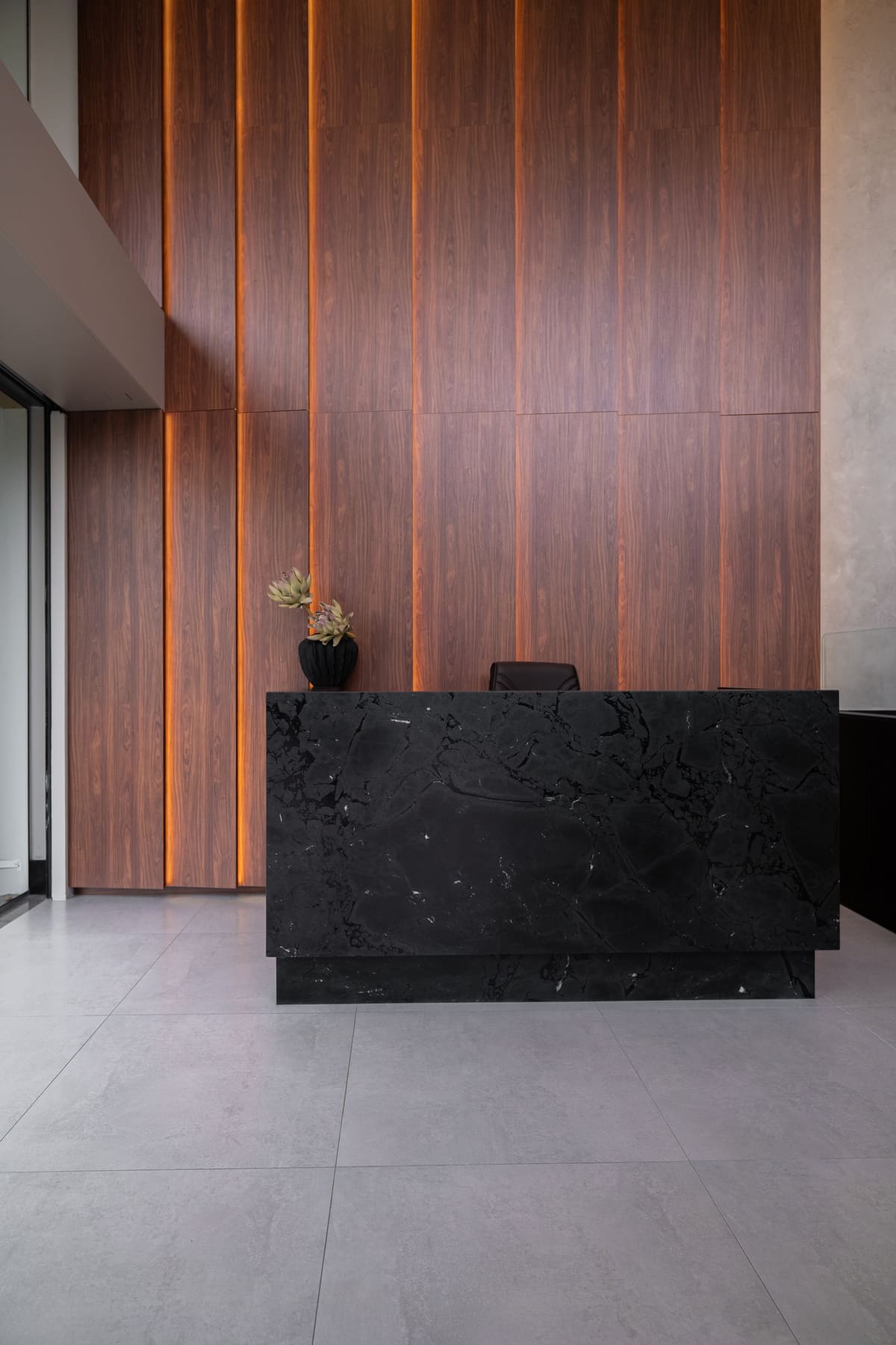 Walnut wall panels with vertical light reveals behind a black stone desk